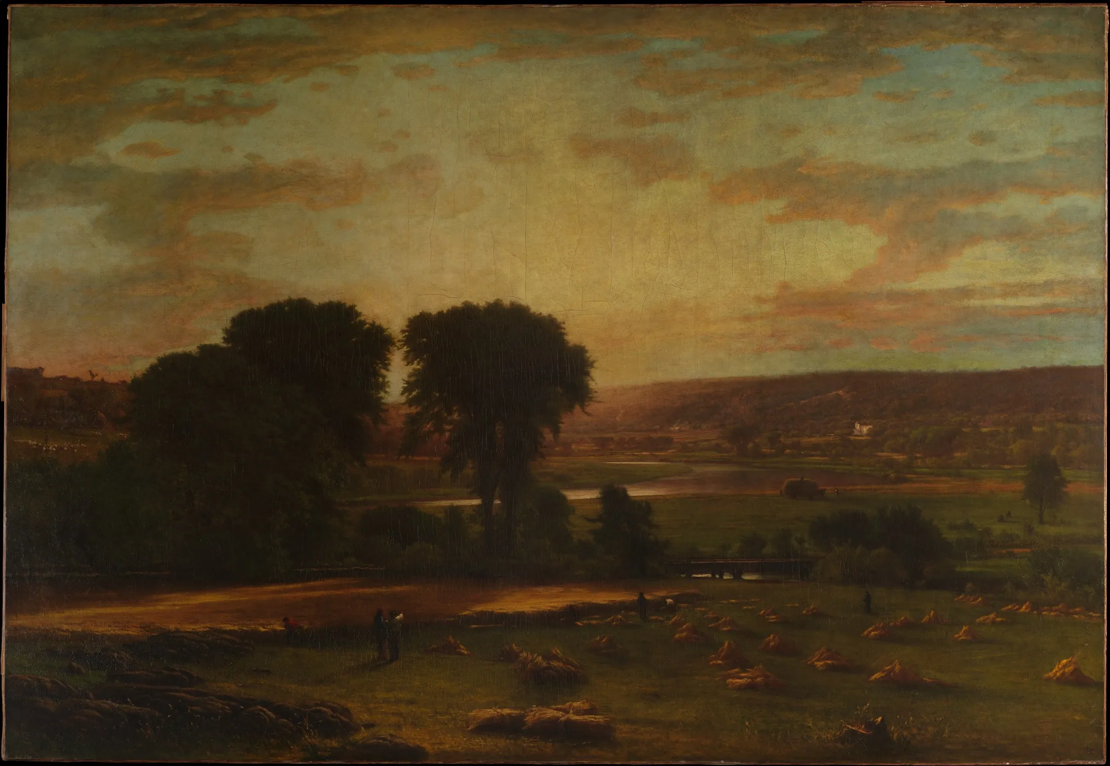A golden harvest landscape with sheaves of wheat, tall trees and a wide, hazy sky.