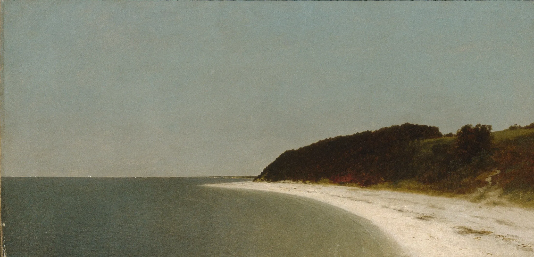 A calm bay with a pale beach and a dark wooded headland under a grey sky.